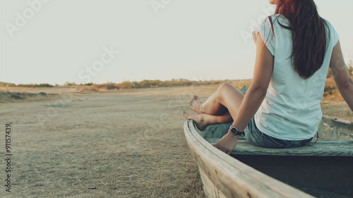 Beautiful girl with long hair sitting on an old tramp boat in photo