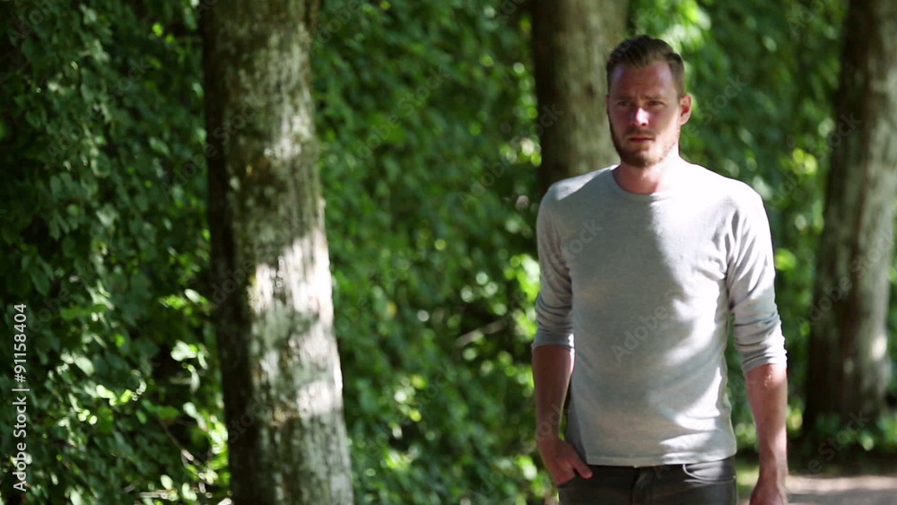 A lonely man wearing a grey shirt, walking in a park on a sunny summer day. Wearing a grey shirt and jeans.