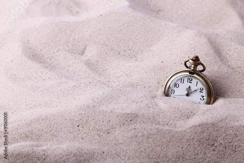 Vintage pocket watch partially buried in the sand