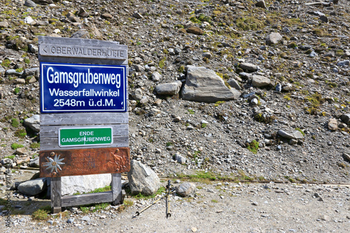 Trekking poles next to a sign indicating the end of Gamsgrube Nature hiking trail along the Pasterze Glacier and the way to waterfall at 2548m above sea leavel at Grossglockner, Austria photo