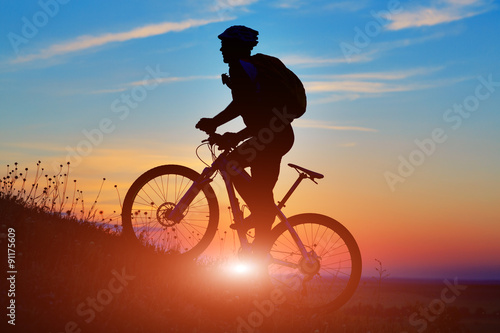 Silhouette of a biker and bicycle on sunset background. © Aleksey
