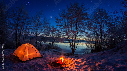 Illuminated tent in the winter camp by the lake at night