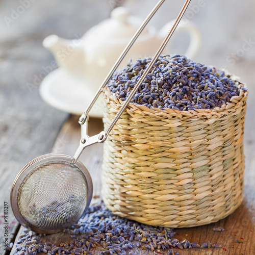 Fotografi Lavender herbal tea in basket, tea infuser and teapot on backgro