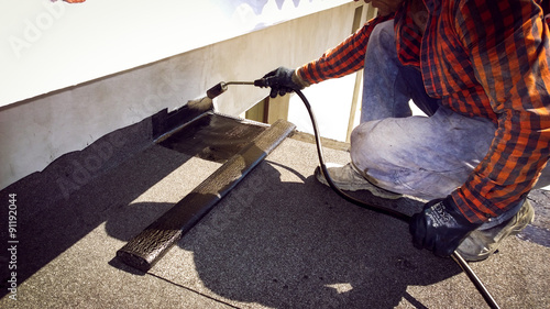Roofer installing a roll of roofing felt by gas blowpipe torch photo