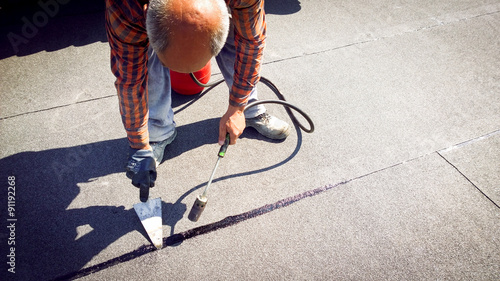 Slika na platnu Roofer installing a roll of roofing felt by gas blowpipe torch