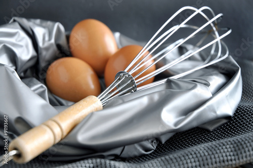 close up whisk with eggs on background