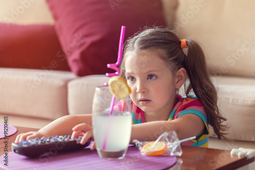 Canvastavla cute little girl with remote changes channel on tv