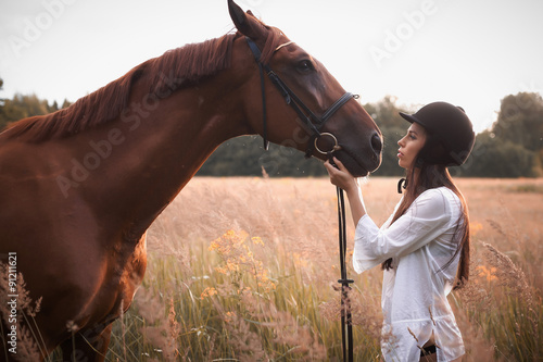 Slim girl in helmet looking at brown horse.