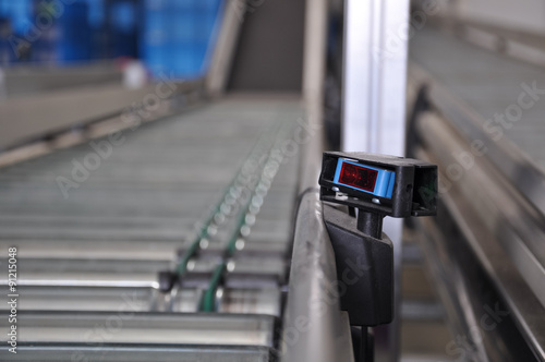 Close up shot of a roller conveyor with a laser distance sensor on the side. Photo taken in a big warehouse. photo