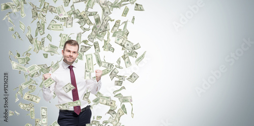 Happy successful manager or businessman is getting benefits from his job. Dollar note are falling down from the ceiling. Concrete background.