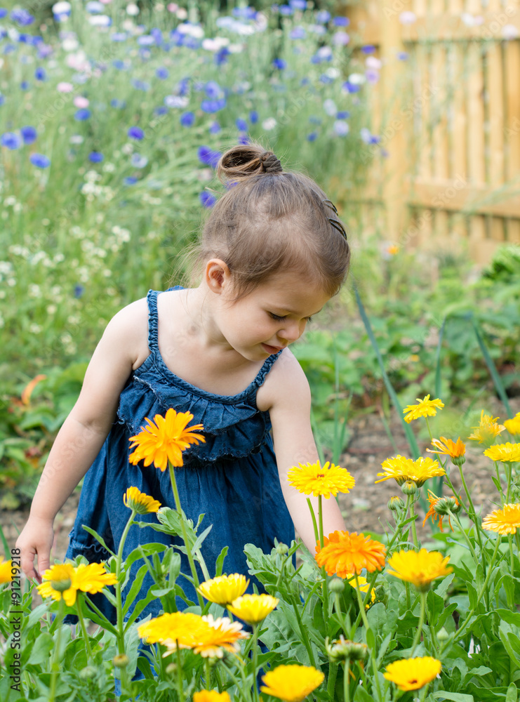 A little girl in a denim sun dress sniffing flowers in the garden A little girl in a denim sun dress sniffing flowers in the garden