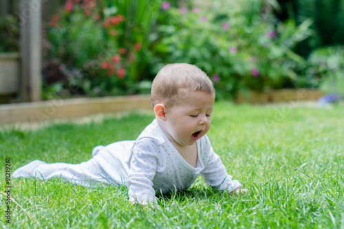 A baby laying on the grass, having tummy time, yawning