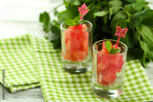 Cold watermelon pieces in glasses, on wooden table background