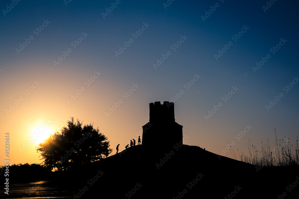 Sunset silhouettes of a medieval church on a hill, tree and peop