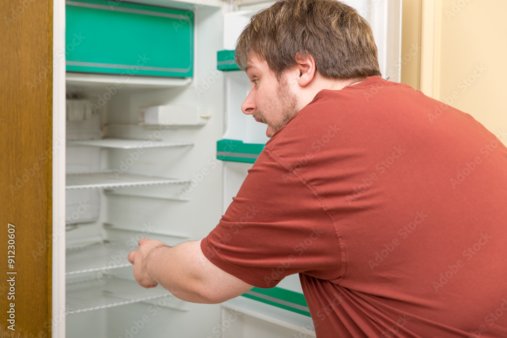 Dicker Mann steht vor leerem Kühlschrank