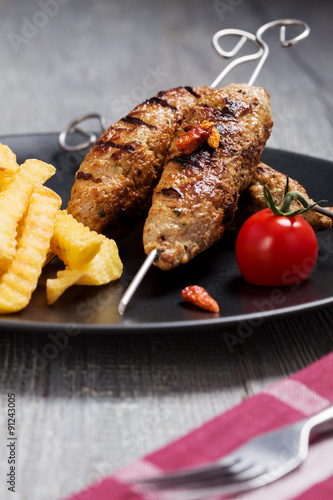 Barbecued kofta - kebeb with fries and vegetables on a plate.