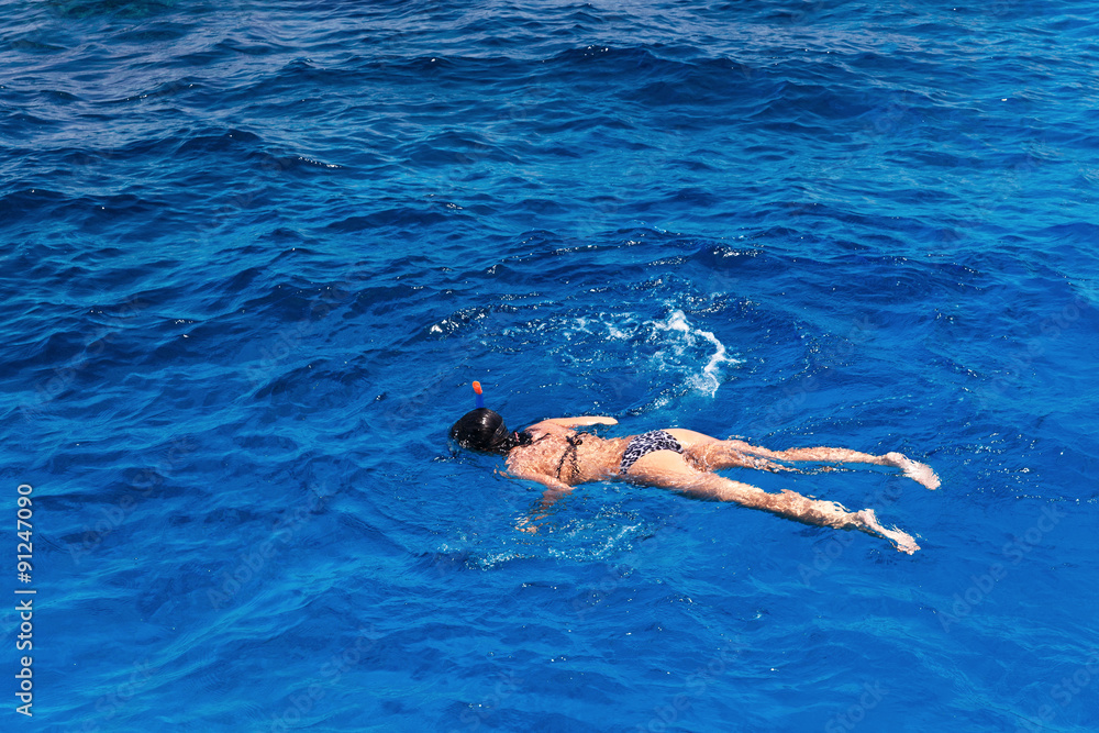 Young woman in swimsuit snorkeling in blue and transparent tropical sea