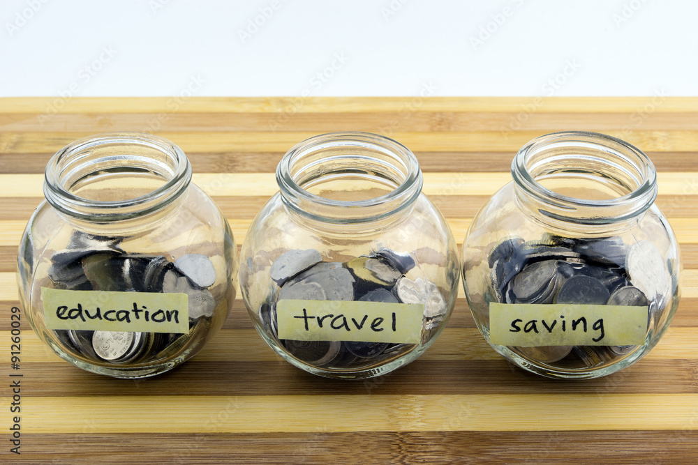 Coins in glass container with travel, saving and education label. Selective focus. Coins in glass container with travel, saving and education label. Selective focus.