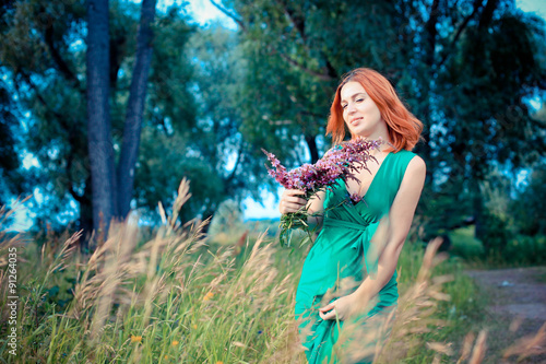 Romantic red-haired young woman in green long dress Walking