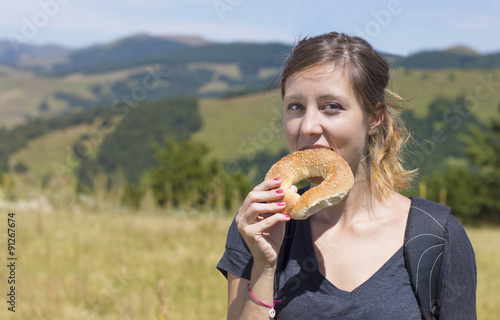 Happy girl hiker eating a doughnut outdoors