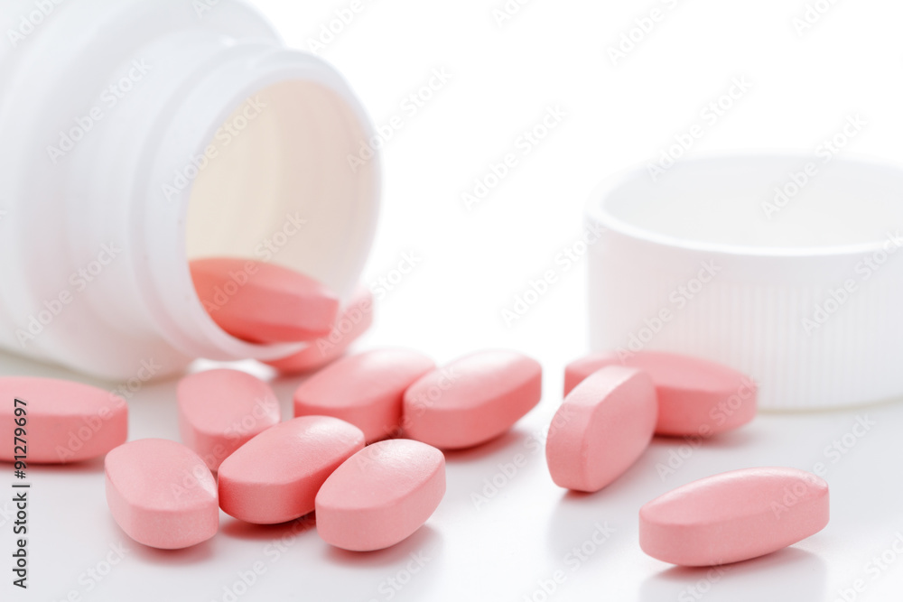 Pink oval pills poured out of a white bottle Pink oval pills poured out of a white bottle