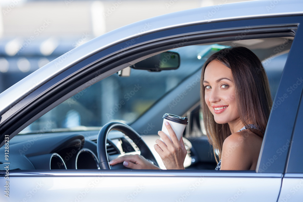 Cute young woman is driving a vehicle with hot drink