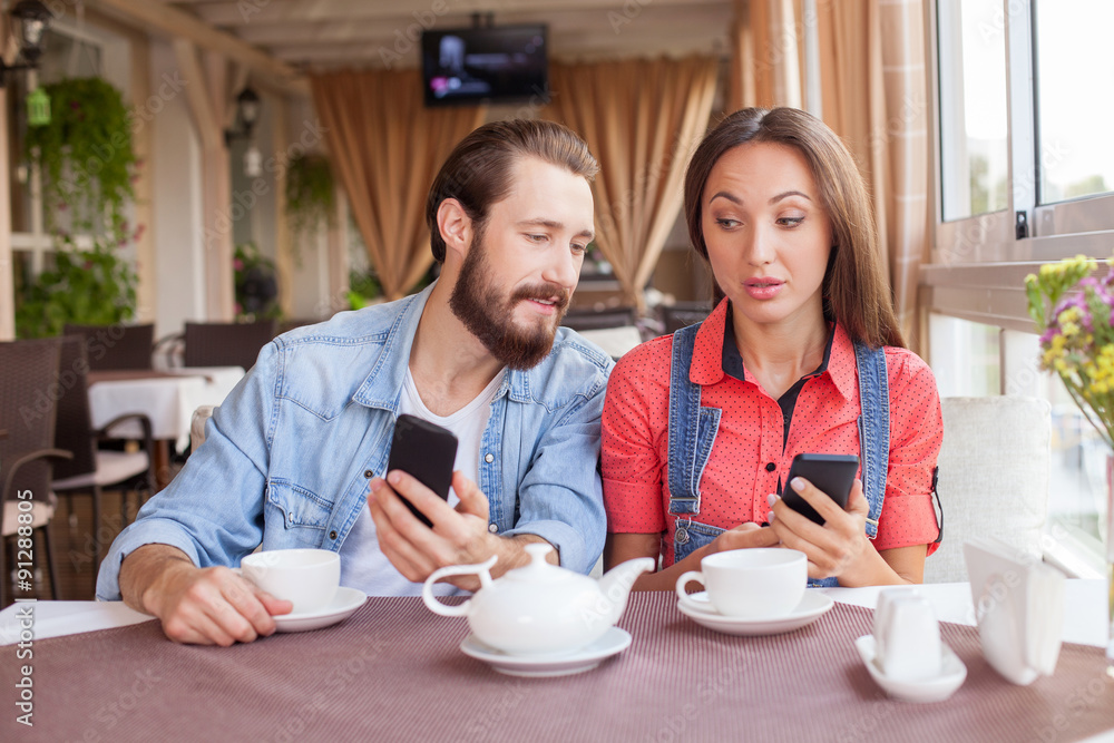 Pretty man and woman are using telephones is cafeteria Pretty man and woman are using telephones is cafeteria