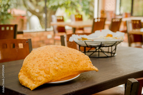 Large empanada on wooden table next to basket of typical latin photo