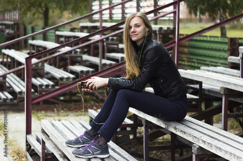 Young beautiful girl look and listening music on your mobile phone on the old stadiums bench photo