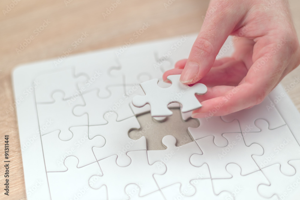 Female hand putting a missing piece into jigsaw puzzle Female hand putting a missing piece into jigsaw puzzle