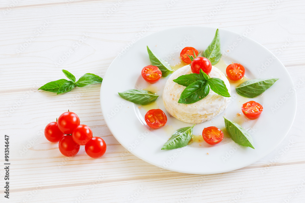 round piece of cheese with basil and cherry tomatoes on a white plate round piece of cheese with basil and cherry tomatoes on a white plate