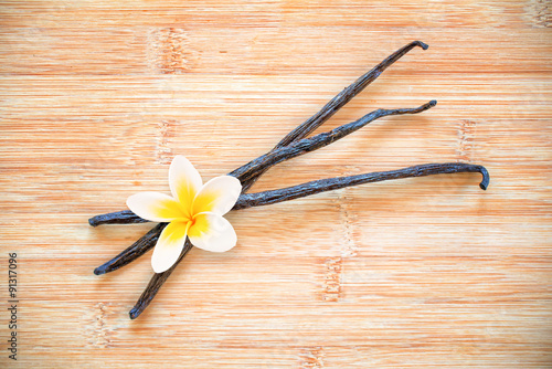 Three vanilla pods with a flower on wooden background