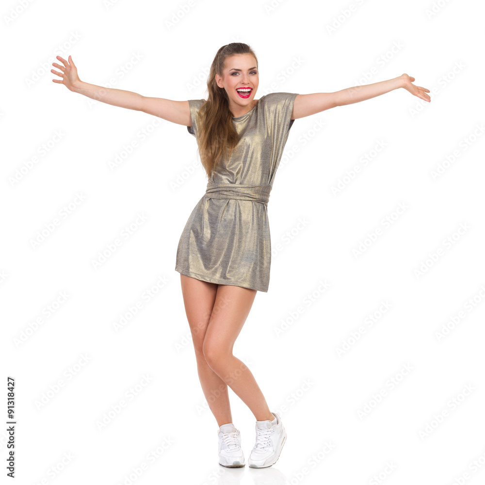 Welcome Everybody. Smiling young woman in gold mini dress and white sneakers standing with arms outstretched. Full length studio shot isolated on white. Welcome Everybody. Smiling young woman in gold mini dress and white sneakers standing with arms outstretched. Full length studio shot isolated on white.