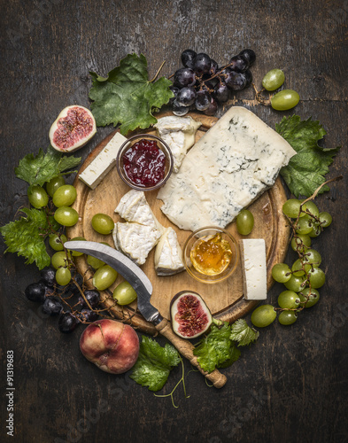 cheese plate with gorgonzola and Camembert cheese with Knife for cheese  white and dark grapes, honey and jam on a wooden cutting board on a dark rustic background top view close up photo