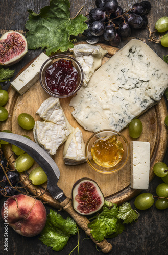 gorgonzola and Camembert cheese with Knife for cheese  white and dark grapes, honey and jam on a wooden cutting board on a dark rustic background top view close up