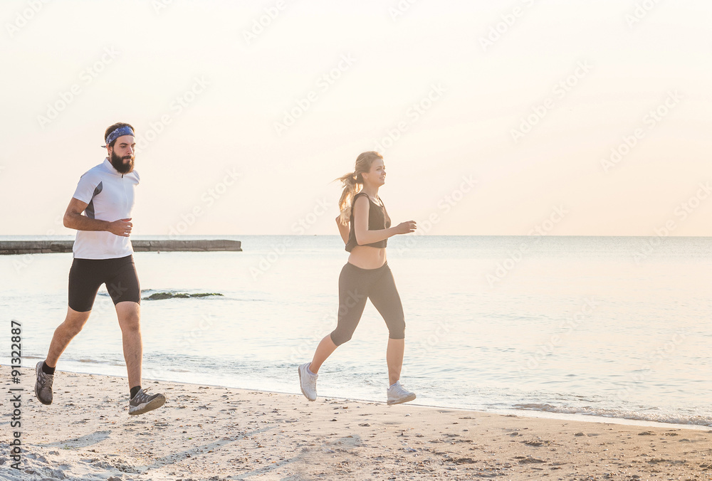 Running people - woman and man athlete runners jogging on beach. Fit young fitness couple exercising healthy lifestyle outdoors during sunrise or sunset