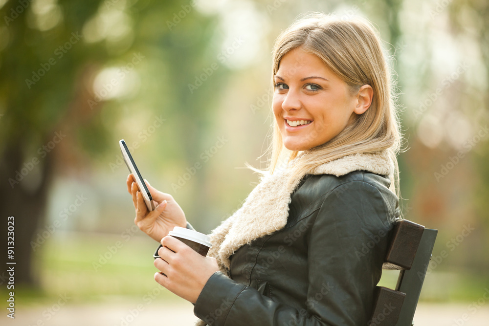 Young woman using tablet in park, drinking coffee to go Young woman using tablet in park, drinking coffee to go
