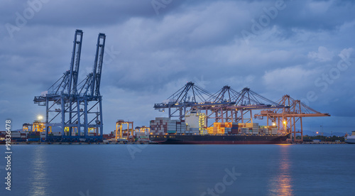 Container Cargo freight ship with working crane bridge in shipyard at dusk for Logistic Import Export background