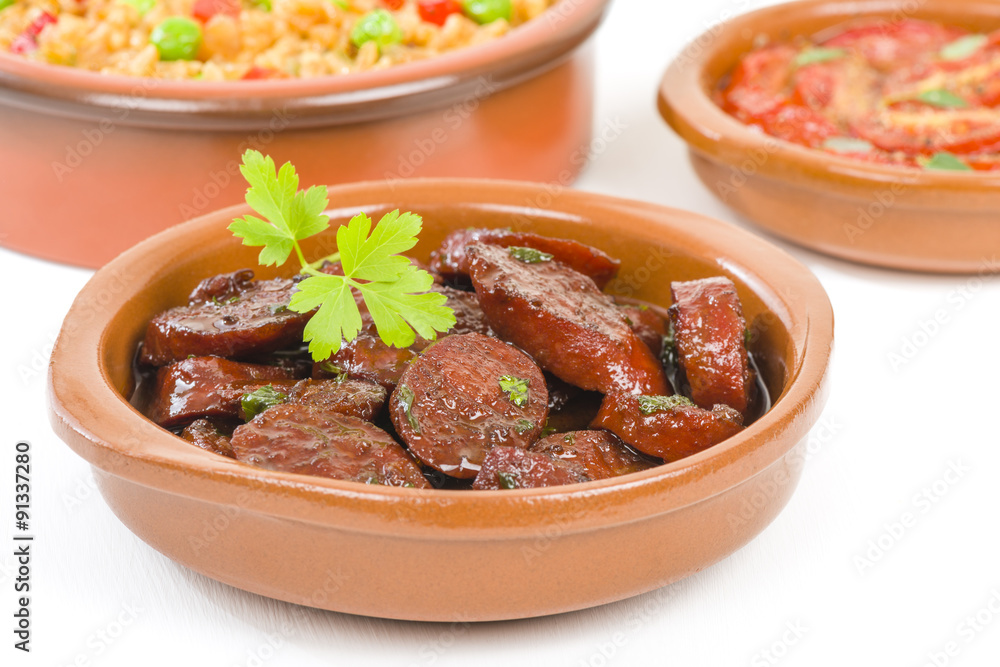 Chorizo al Vino (Spicy sausage cooked in red wine). Traditional Spanish tapas dish. Other tapas dishes on background.
