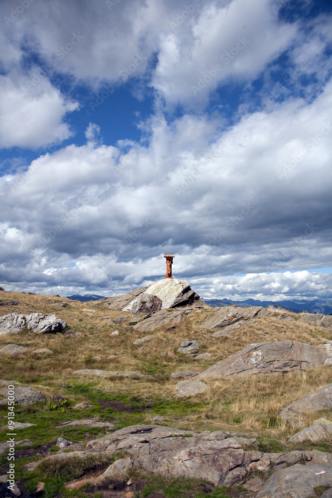 A wooden sculpture placed in the high mountains with blue sky and clouds