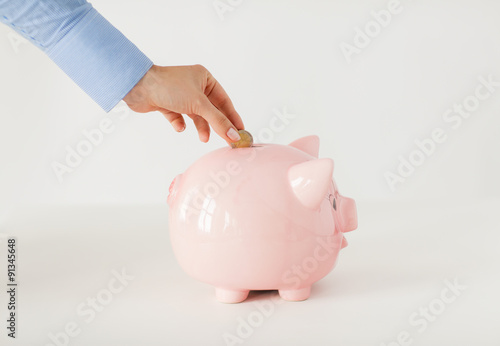 close up of hand putting coin to piggy bank