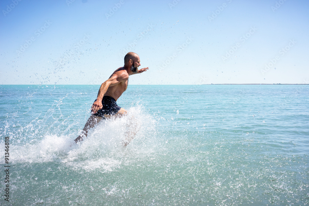 A strong man, athletic, running fast on the ocean with a naked torso
