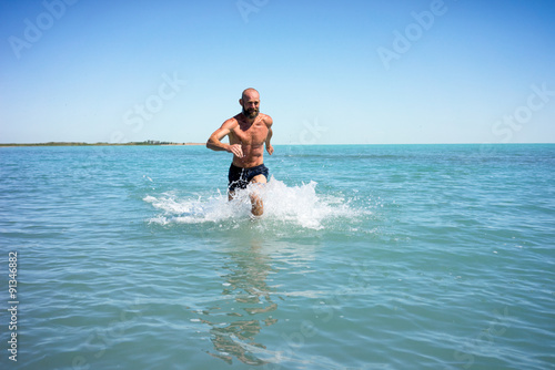 Bald middle-aged man running fast on the lake with a naked torso