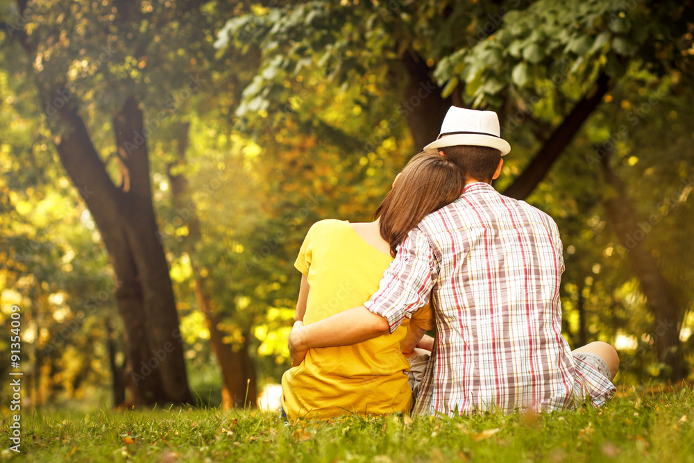 Rearview of an affectionate young couple sitting in park Rearview of an affectionate young couple sitting in park
