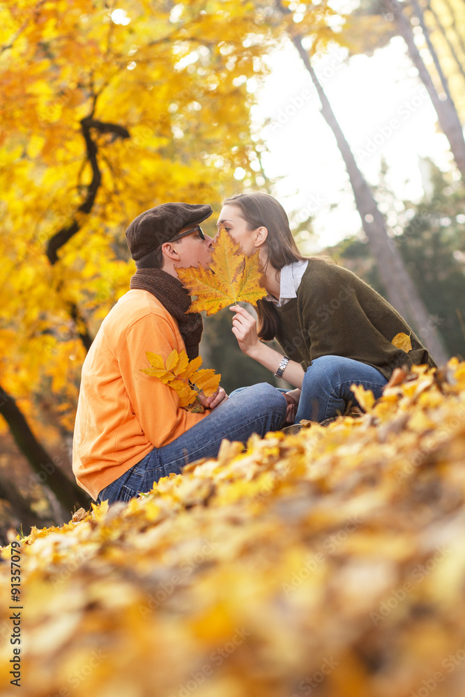 Young couple kissing in the park while hiding the kiss with leaf. Young couple kissing in the park while hiding the kiss with leaf.