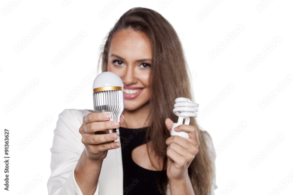 smiling young woman holding LED bulb and fluorescent bulb smiling young woman holding LED bulb and fluorescent bulb