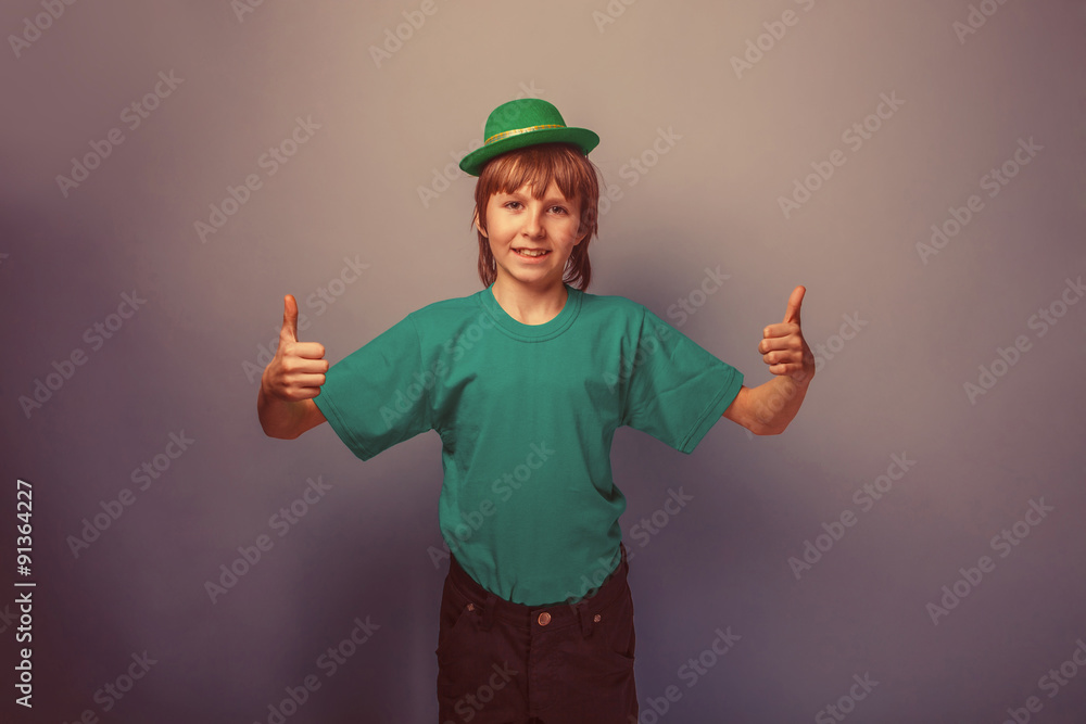 European-looking boy of ten years thumbs up in a hat on a gray b