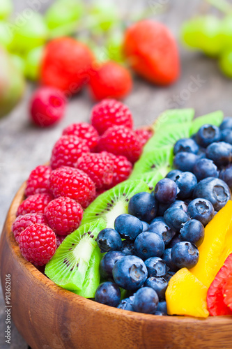 Fresh colorful fruits and berries in wooden bowl on rustic table