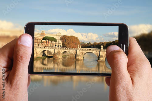 Canvas Print Male hand taking photo of river Tiber from the bridge in Rome with cell, mobile phone