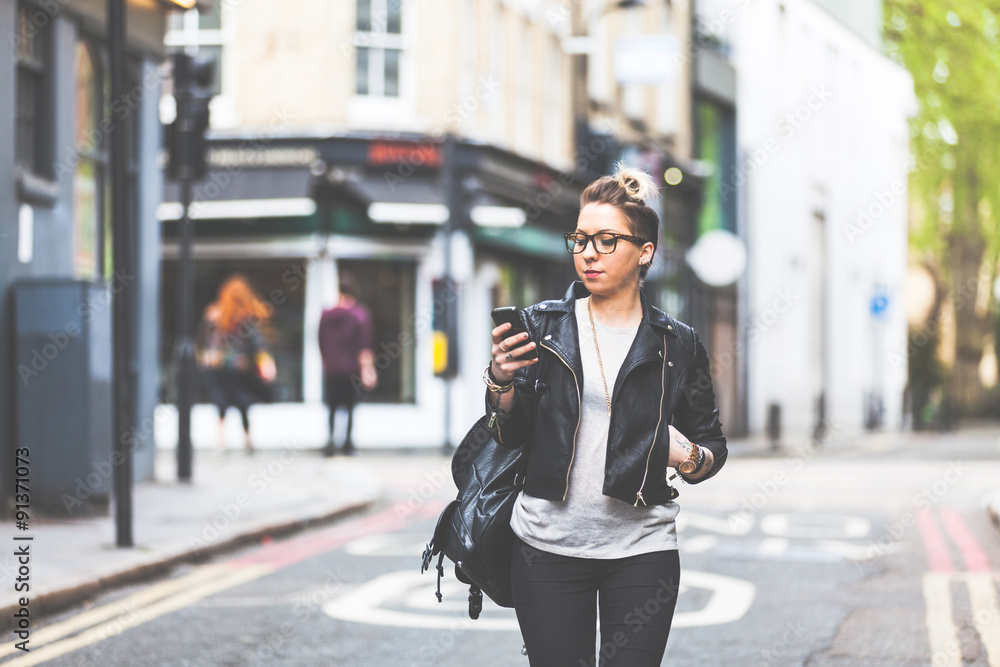 Girl walking down the street with her phone. - obrazy, fototapety, plakaty 